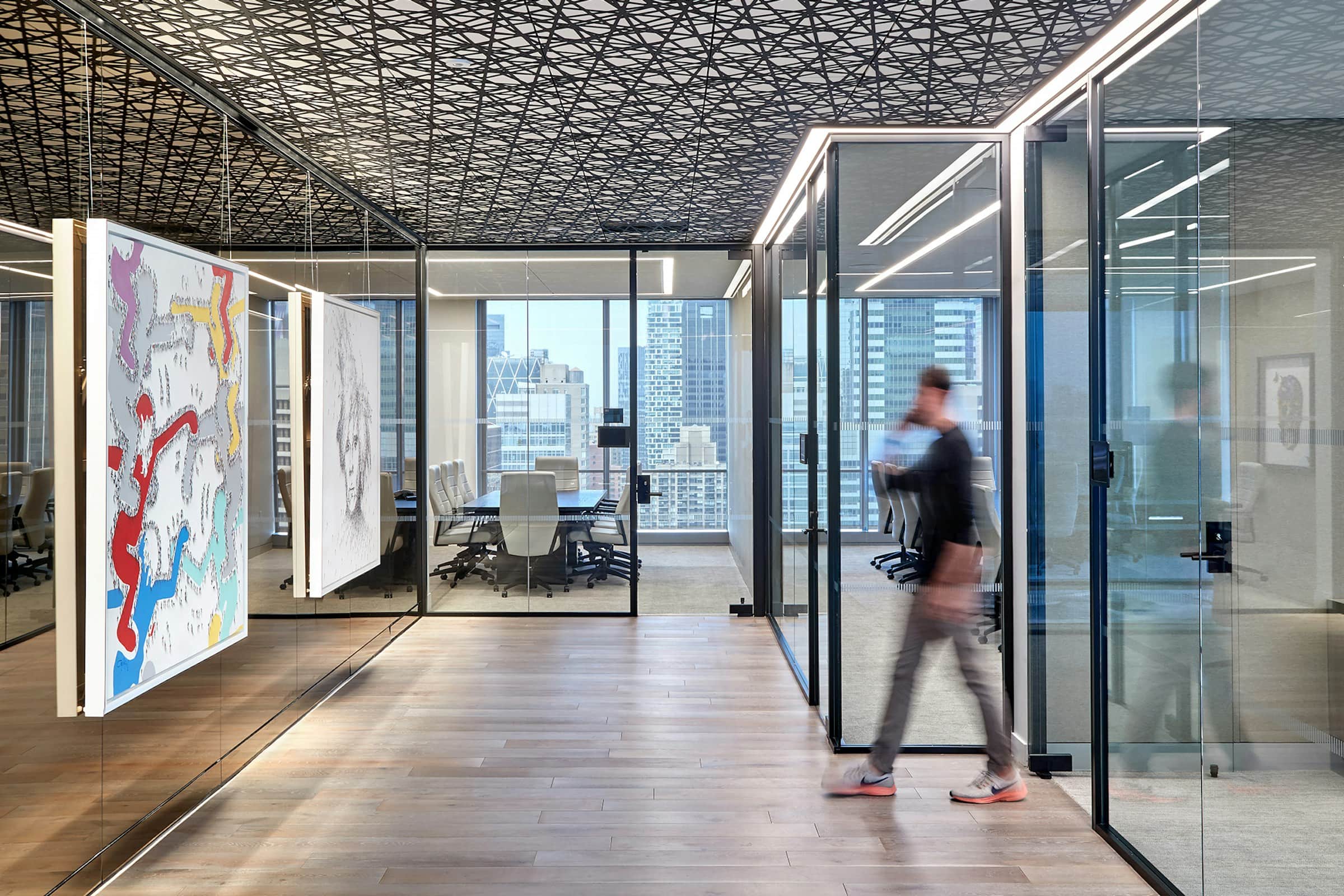 Executive office with glass-front conference rooms, wood floors, and a person walking through, city skyline beyond